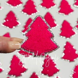 May include: A close-up of a pink felt Christmas tree with a silver glitter outline. The tree is being held by a hand. The text "Stitched Originals" is visible in the background.