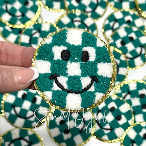 May include: Green and white checkered smiley face patch with a gold glitter trim. The patch is made of a soft, fuzzy material.