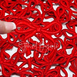 May include: A close-up of a large quantity of red felt bows. The bows are arranged in a random pattern and are all the same size. The bows are perfect for adding a touch of festive cheer to any project.