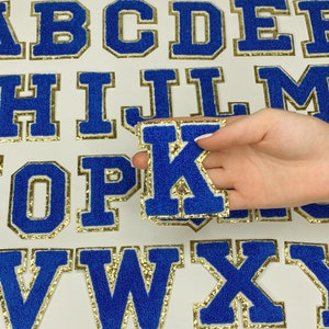 May include: Blue felt letters with gold glitter trim. The letters are in uppercase and are arranged in alphabetical order. The letters are on a white background.