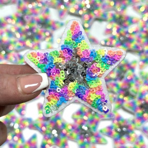May include: A rainbow sequin star patch with a white felt backing. The star is made of iridescent sequins in a variety of colors, including pink, blue, green, and yellow.