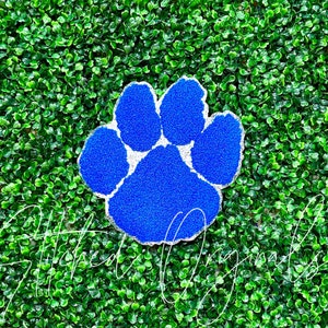 May include: A blue paw print with white accents, made of a textured material. The paw print is on a green background.