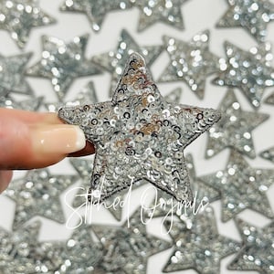 May include: Silver sequin star-shaped patches. The stars are approximately 2 inches in diameter and are made of silver sequins sewn onto a fabric backing.