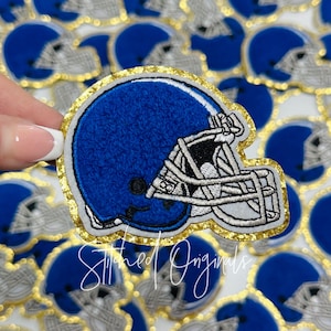 May include: Blue and white embroidered football helmet patch with a gold glitter outline. The patch is made of felt and has a stitched design.