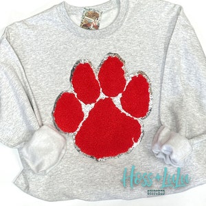 May include: Gray sweatshirt with a large red sequin paw print. The sweatshirt has the text "Hoss + Lula Stitched" in teal lettering on the bottom.