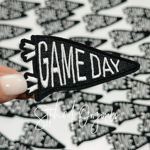May include: Black and white embroidered iron-on patch shaped like a pennant with the text "GAME DAY" in white.