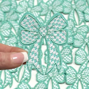 May include: A collection of green and white checkered bow appliques. The bows are made of fabric and have a stitched design.