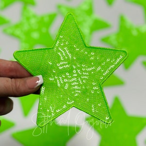 May include: A bright green star-shaped patch covered in sequins. The sequins are white and create a sparkly effect. The patch is sewn with a white thread around the edges.