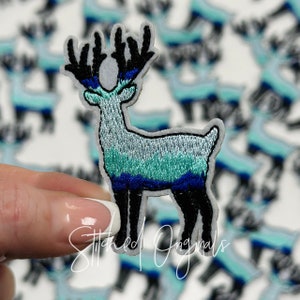 May include: A blue and green embroidered iron-on patch of a reindeer with black antlers. The patch is on a white background and has the text "Stitched Originals" at the bottom.