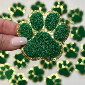 May include: Green and gold glitter paw print iron-on patch. The paw print is made of a fuzzy green fabric with a gold glitter outline.