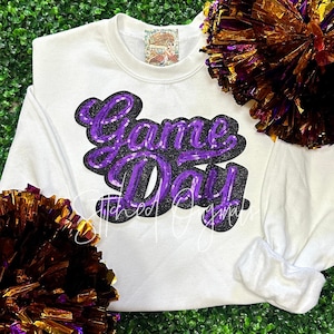May include: White long-sleeve sweatshirt with a purple and black sequined "Game Day" graphic.