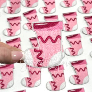 May include: Pink felt Christmas stocking patches with white trim and pink zig-zag stitching. The patches are approximately 2 inches tall.