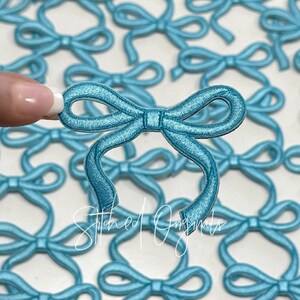 May include: A close-up of a teal blue fabric bow. The bow is made of a soft, velvety material and has a simple, elegant design. The bow is perfect for adding a touch of whimsy to any project.
