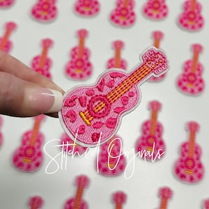 May include: Pink and yellow embroidered guitar patch with a floral design. The patch is surrounded by other guitar patches.