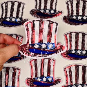 May include: Patches of Uncle Sam hats with red, white, and blue sequins. The hats have a blue brim and white stars. The hats are arranged on a white surface. The patches are for patriotic themed crafts.