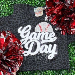 May include: A black and white leopard print t-shirt with a white and silver glitter applique that says "Game Day" with a rhinestone baseball on top.
