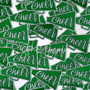 May include: A collection of green megaphone-shaped patches with the word "CHEER" in silver glitter lettering. The patches are scattered across a white background, creating a festive and energetic design. The patches are likely for cheerleading or spirit wear.