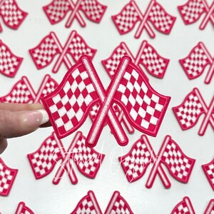 May include: A close-up of a pink and white checkered racing flag patch. The patch is embroidered and has a white border. The patch is shown against a white background.