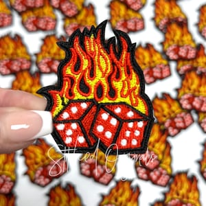 May include: A red and white dice with flames on top. The dice are on fire. The flames are yellow and orange. The dice are embroidered.
