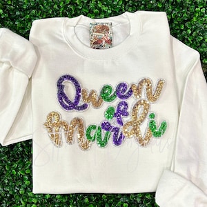 May include: White sweatshirt with a gold, green, and purple sequined design that says "Queen of Mardi Gras".