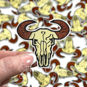 May include: A yellow embroidered bull skull patch with brown horns. The patch is iron-on and perfect for adding a western touch to clothing, bags, or other accessories.