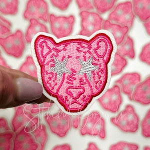 May include: Pink embroidered iron-on patch of a tiger face with silver glitter stars for eyes.