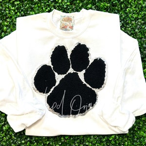 May include: White long-sleeved sweatshirt with a black paw print outlined in silver glitter.