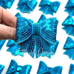 May include: A set of turquoise blue sequin bows. The bows are sewn with a satin stitch and have a shiny finish.