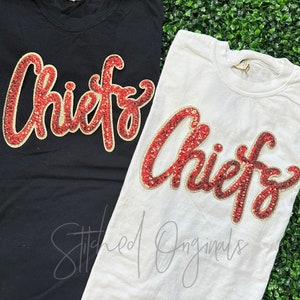 May include: Two t-shirts with the word "Chiefs" in red and gold sequins. The shirts are black and white.