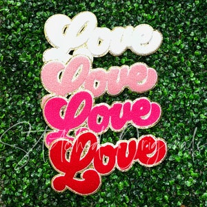 May include: Four felt "Love" signs in different sizes and colors. The signs are white, pink, hot pink, and red. Each sign has a gold glitter outline.