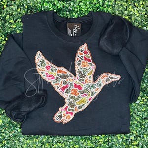 May include: Black sweatshirt with a colorful, beaded bird design. The bird is flying and has a long neck and beak. The sweatshirt has a small tag with the text "Hogs +" on it.