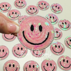 May include: Pink sequin smiley face patches with a silver outline. The patches are approximately 2 inches in diameter.