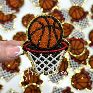 May include: A close-up of a gold glitter basketball with a red and white net. The basketball is in a hoop with a gold glitter rim. The basketball is brown and orange.