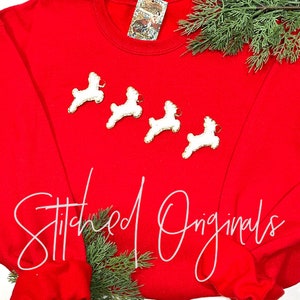 May include: Red sweatshirt with four white reindeer appliques and the text "Stitched Originals" in white.