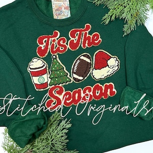 May include: Green sweatshirt with the text "Tis the Season" in red and gold glitter. The sweatshirt has embroidered images of a Christmas tree, a football, a coffee cup, and a Santa hat.