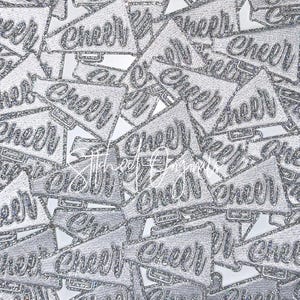 May include: A pattern of silver glitter megaphone shapes with the word "Cheer" in a script font. The megaphones are layered and overlapping, creating a textured, sparkling effect. The background is white.
