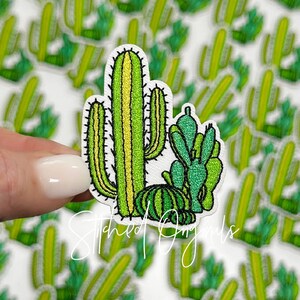 May include: Green embroidered cactus patch with a tall, slender cactus and a smaller, round cactus. The patch is perfect for adding a touch of desert charm to your projects.