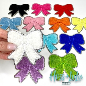 May include: Assortment of felt bow patches with silver glitter trim. The bows are in various colors including black, pink, red, blue, white, orange, yellow, green, and purple.