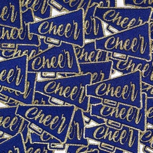 May include: A collection of navy blue megaphone-shaped patches with gold glitter lettering that spells "CHEER". The patches have a gold glitter border and are scattered across a white background. These patches are ideal for cheerleading apparel.