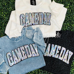 May include: Three sweatshirts with the word "GAMEDAY" in rhinestones. The sweatshirts are white, light blue, and black with a leopard print.