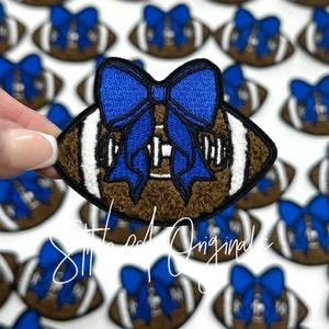 May include: Brown and white football with a blue bow on top. The football is fuzzy and the bow is made of fabric.