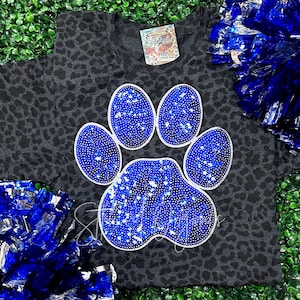 May include: A gray t-shirt with a black leopard print design. A large blue paw print with silver glitter is centered on the shirt.