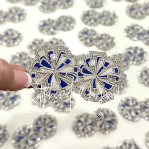 May include: Two silver glitter iron-on patches with a blue and white embroidered design. The design is a stylized flower with a circular shape.