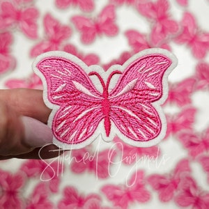 May include: Pink felt butterfly applique with white stitching. The butterfly has a detailed design with multiple lines and curves.