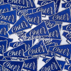 May include: A collection of blue megaphone-shaped patches with the word "CHEER" in silver glitter script. The patches are scattered across a white background, creating a textured, celebratory design.