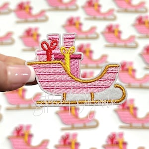May include: Pink and gold embroidered Christmas sleigh with presents. The sleigh is decorated with gold trim and has a white base.