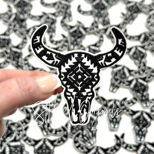 May include: Black and white embroidered bull skull patch with a geometric pattern. The patch is iron-on and can be used to decorate clothing, bags, and other items.