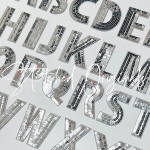 May include: A set of silver and black sequined letters of the alphabet. The letters are arranged in alphabetical order and are on a white background.