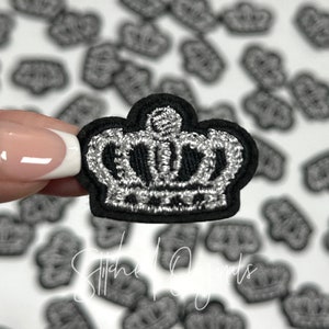 May include: A silver and black embroidered crown patch. The crown has a pointed top and five points on the crown. The patch is about 1 inch in diameter.