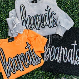 May include: Three sweatshirts with the word "bearcats" in rhinestones on the front. The sweatshirts are in gray, orange, and black.